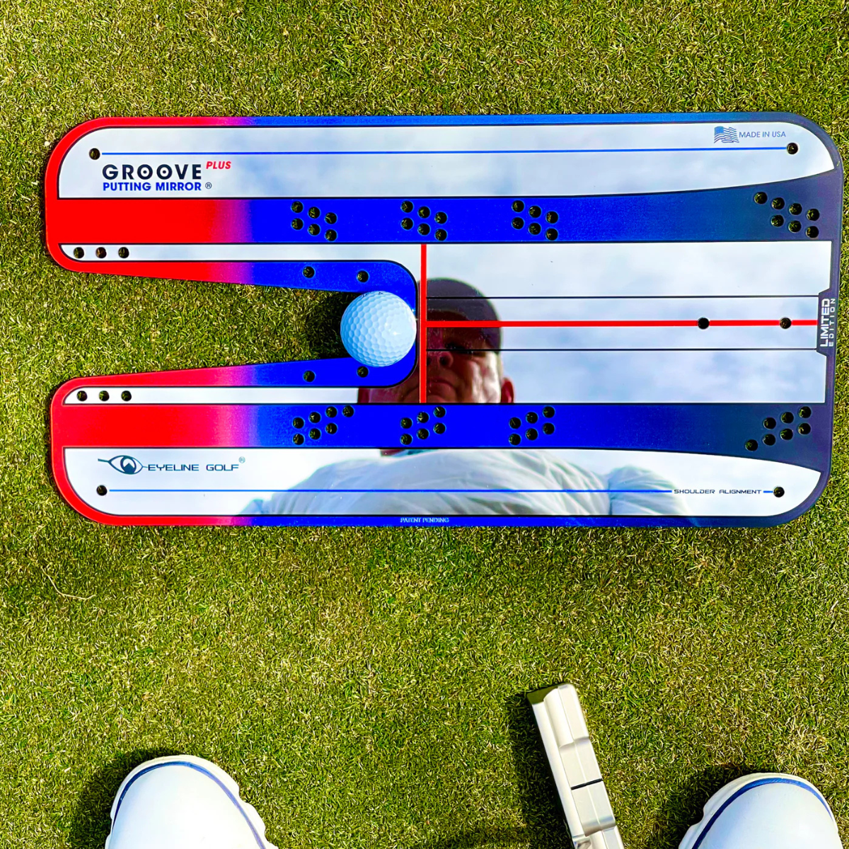 Golf putting mirror on grass with a golf club and shoes in the foreground