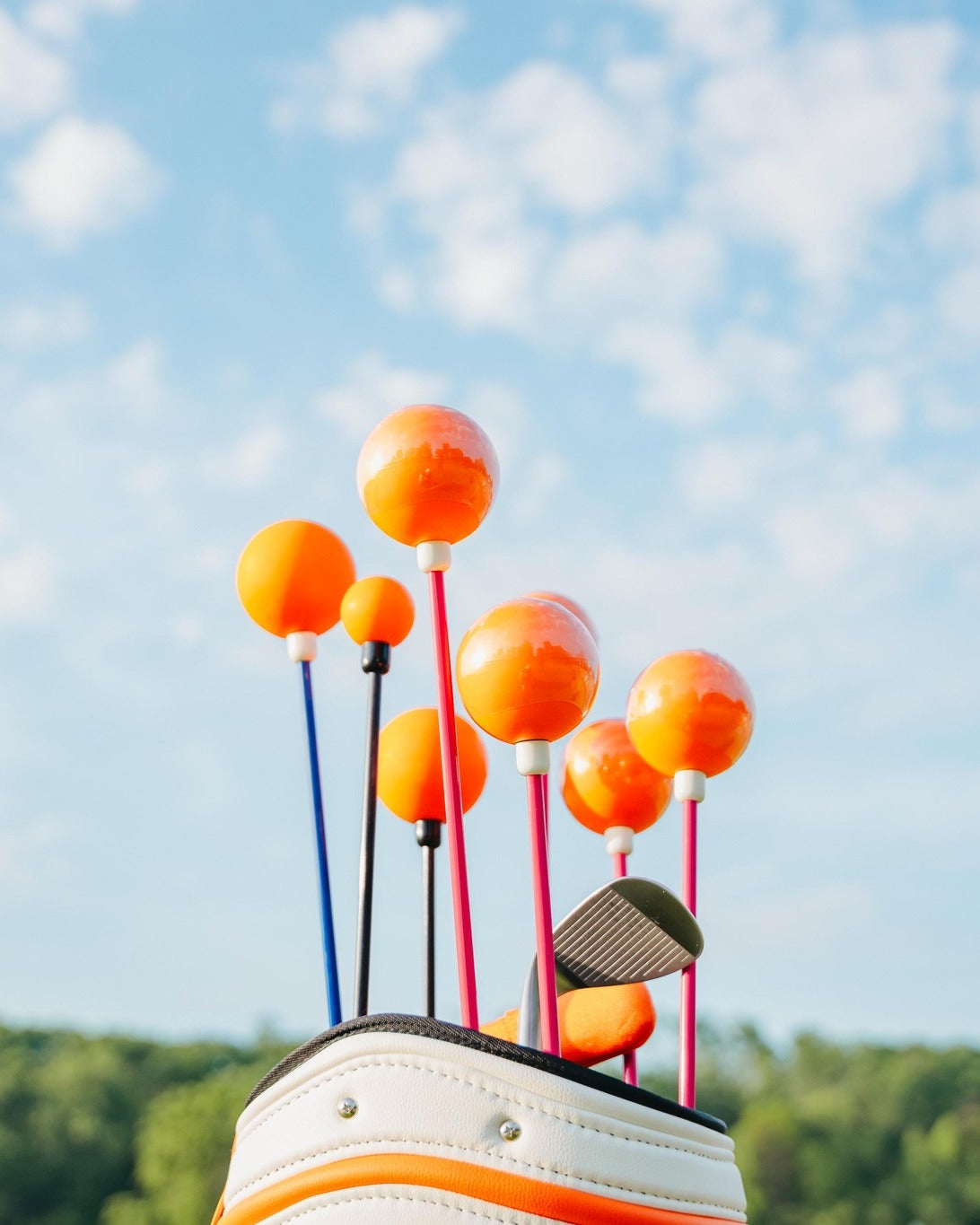 Golf club with orange driver heads against a blue sky