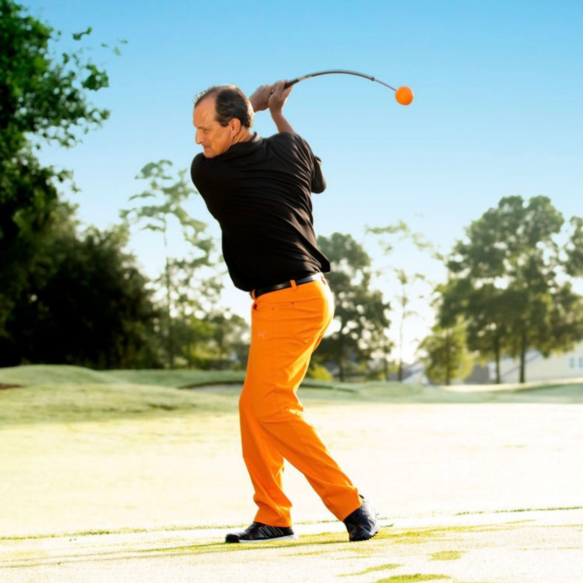 Man in black shirt and orange pants playing golf on a sunny day.