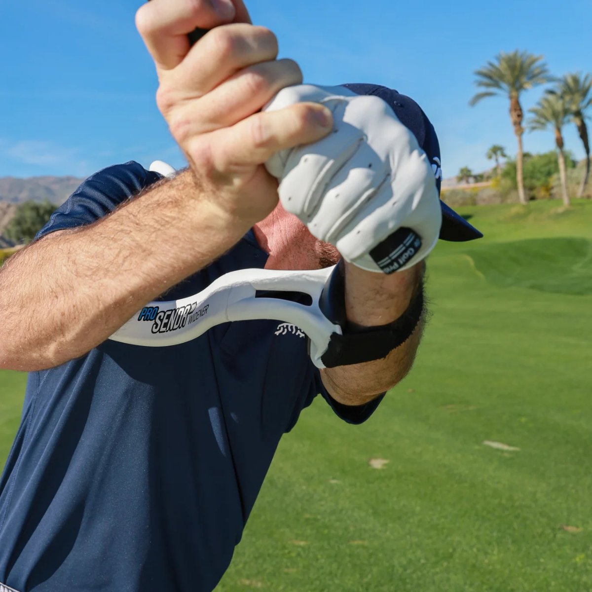Person holding a golf club and using the ProSENDR Widener on a golf course with palm trees in the background