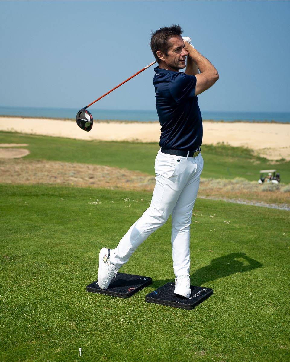 Man playing golf with the Smart2Move on a green course with a clear blue sky.