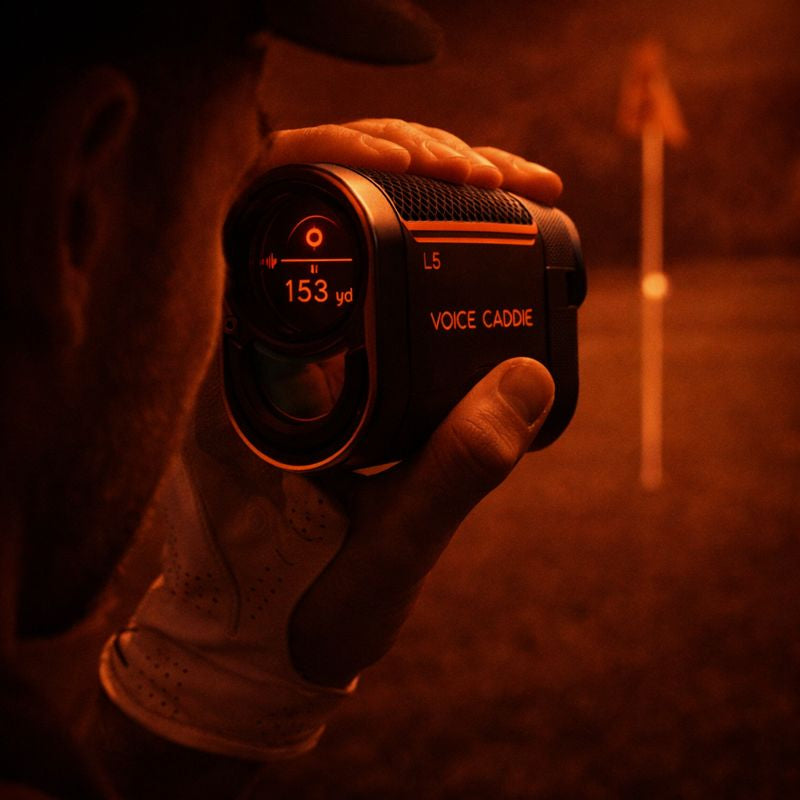 Close-up of a Voice Caddie laser rangefinder locking onto a flagstick, highlighting precise distance measurement in low light.
