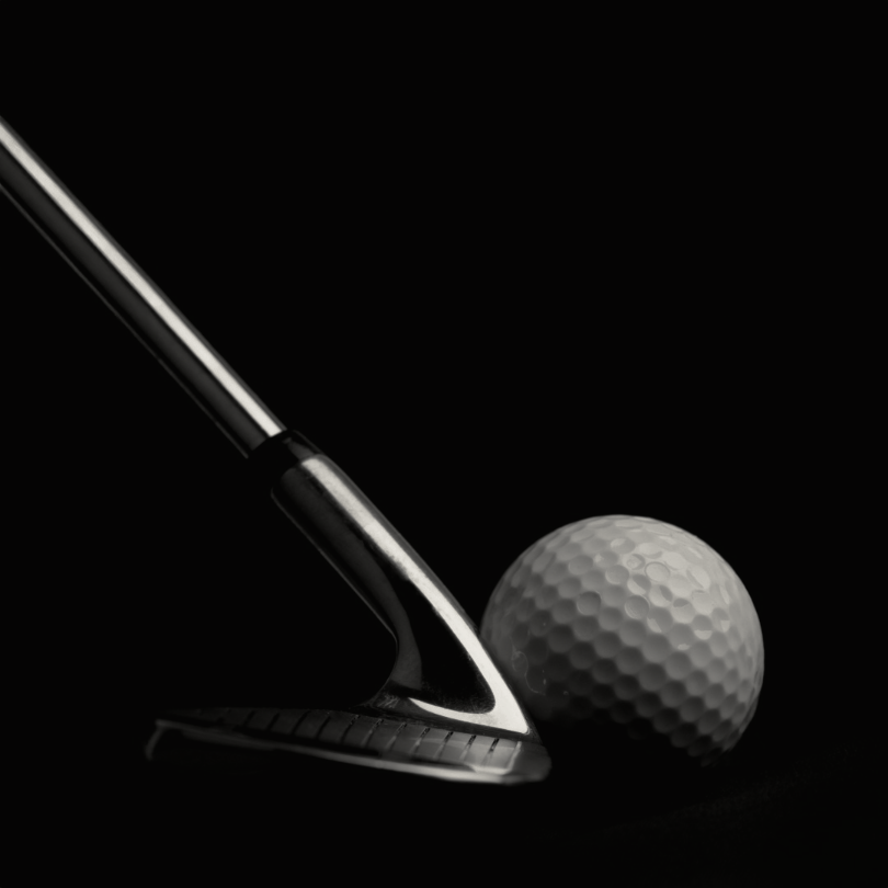Close-up of a golf putter striking a golf ball against a dark background.