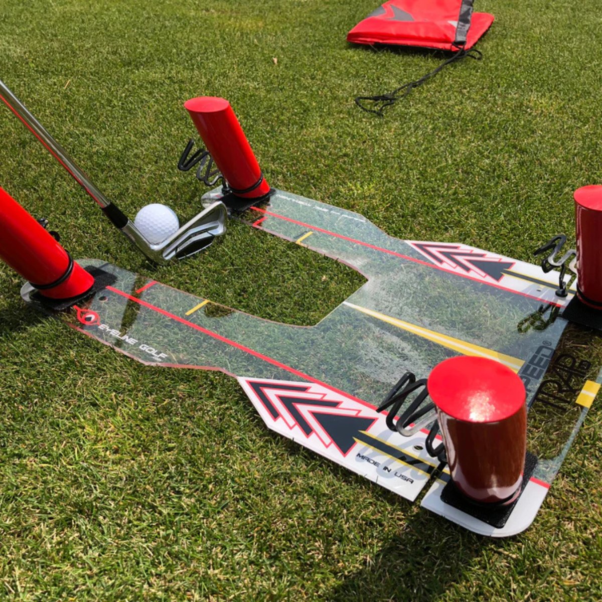 Golf practice device with red stands and a white ball on grass