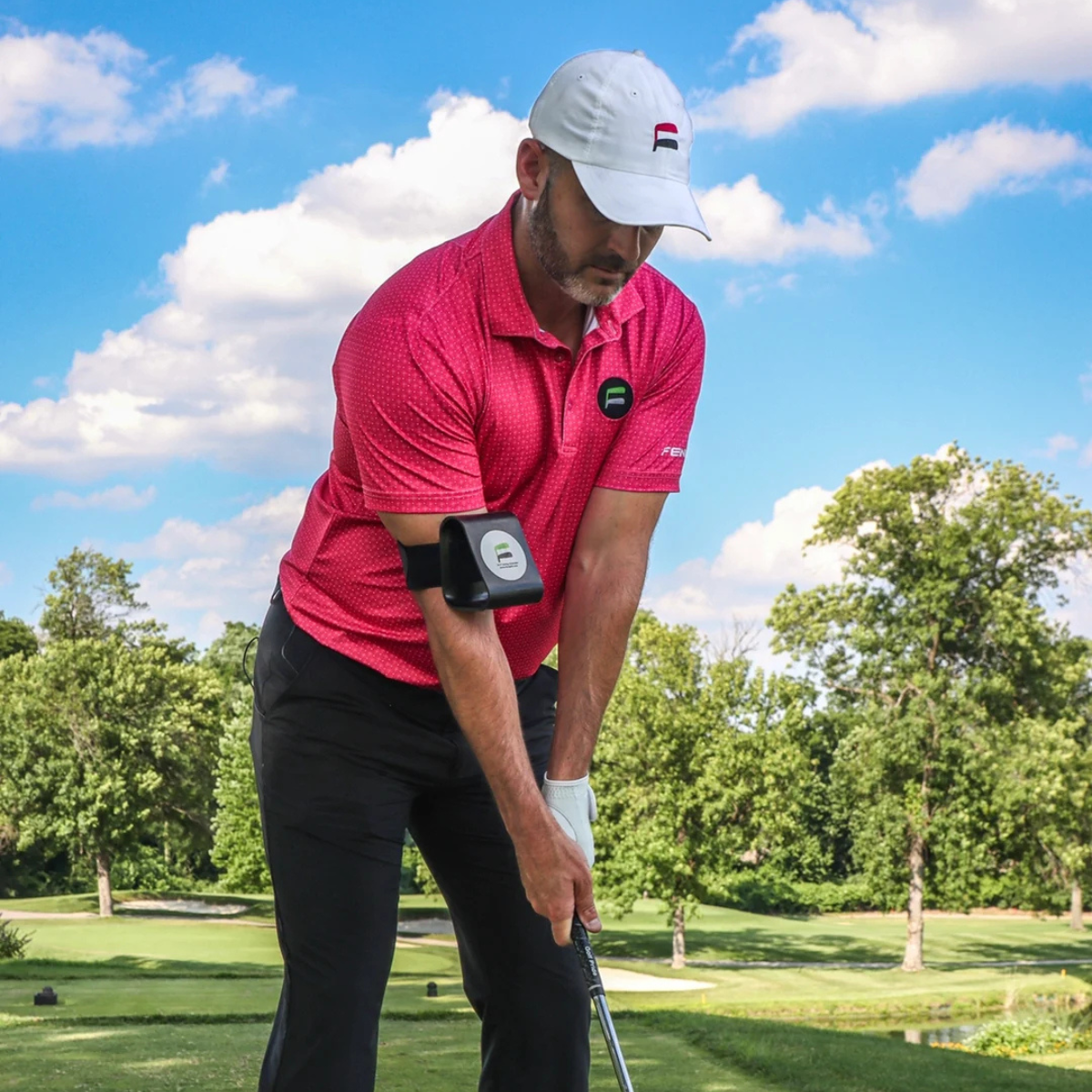 Man in pink shirt and white cap playing golf on a sunny day with the Flyt Golf Swing Extender