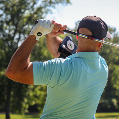 Man in light blue shirt and black cap swinging a golf club with the Flyt Golf Swing Extender with trees in the background