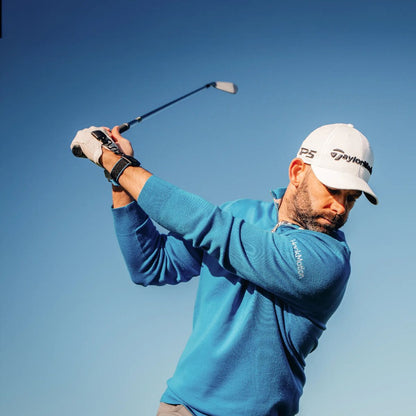 Man swinging a golf club against a clear blue sky