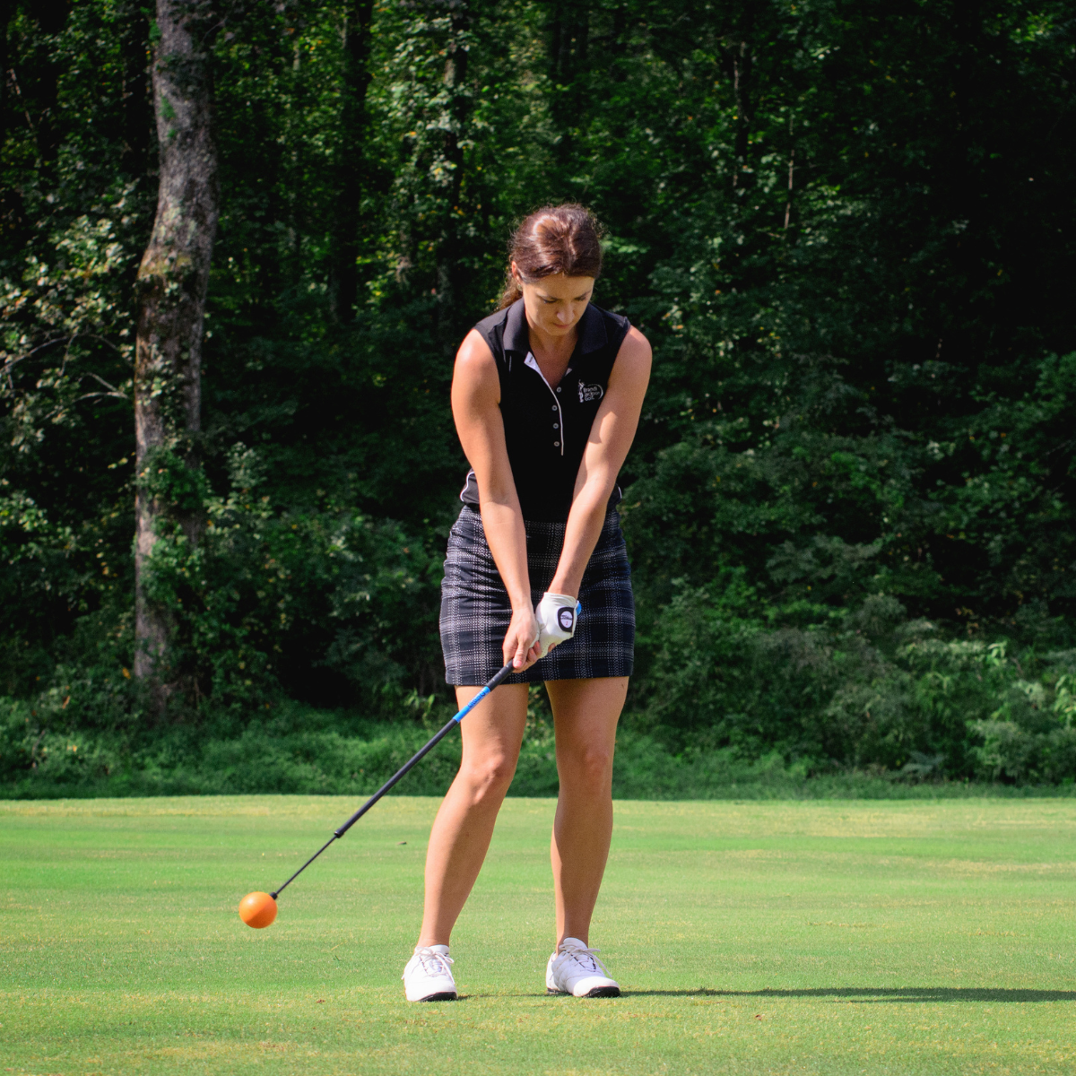 Woman playing golf on a green course with trees in the background