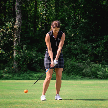 Woman playing golf on a green course with trees in the background
