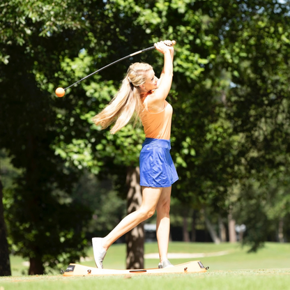 Woman playing golf with the Orange Whip on a sunny day with trees in the background