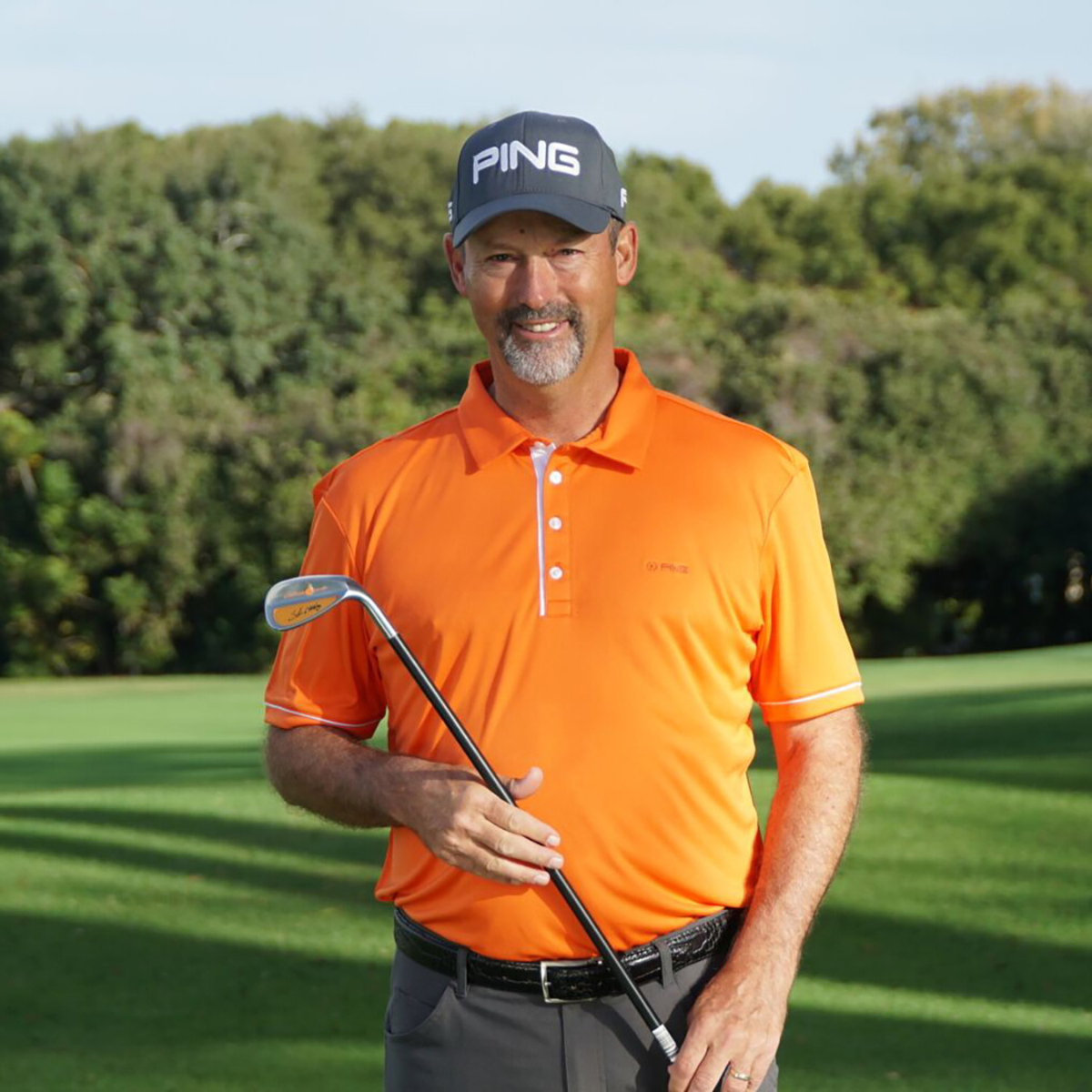 Man in orange shirt and blue cap holding the Orange Whip Wedge on a golf course