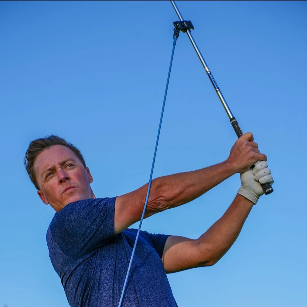 Man swinging a golf club with the  PlaneMate against a clear blue sky
