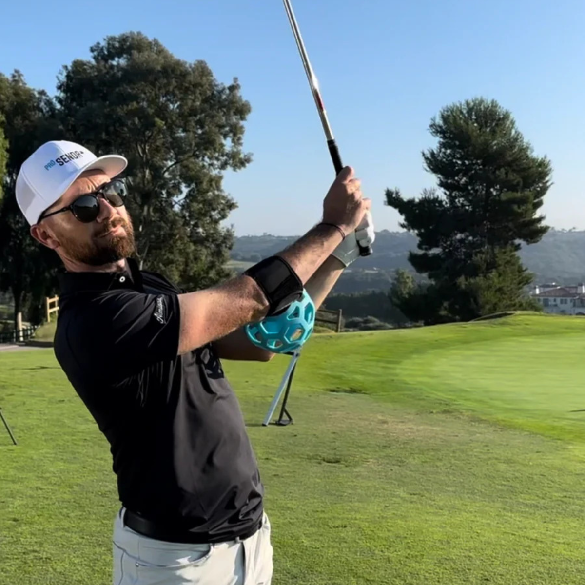 Man playing golf on a green course with trees and clear sky in the background