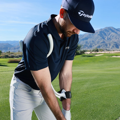 Golfer in a blue shirt and cap on a golf course with mountains in the background