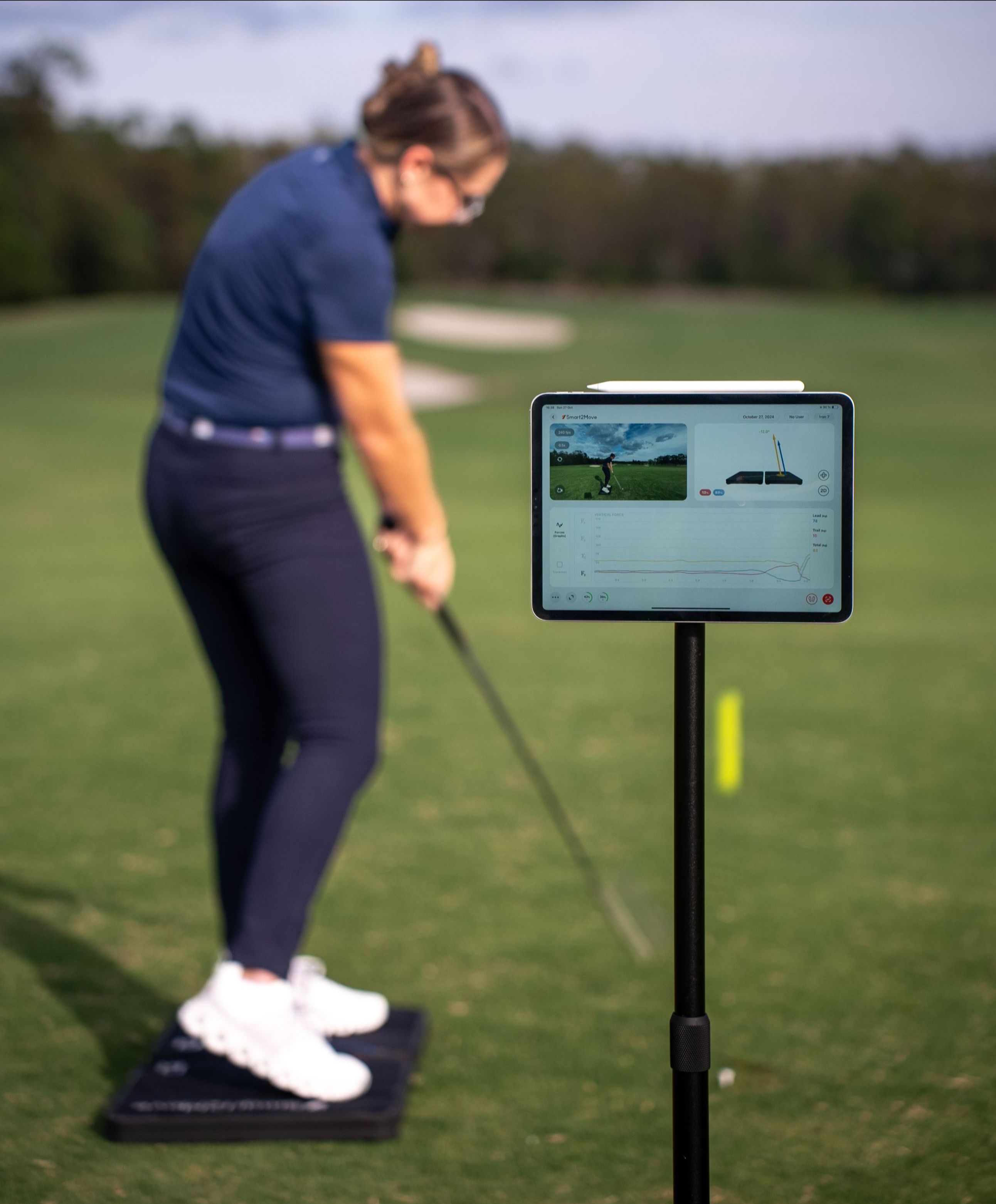 Person on a golf course using a device displaying a video of a golf swing.