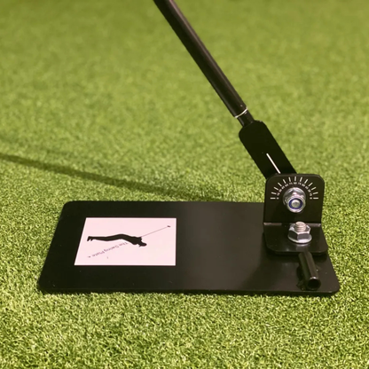 Golf swing trainer on a green surface with a black mat displaying The Swing Plate logo