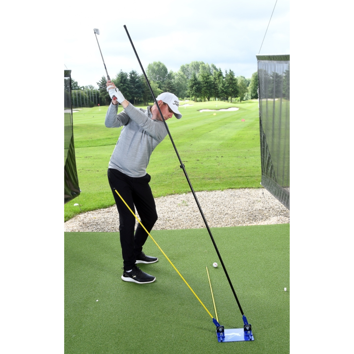 Person practicing golf swing with a golf training device on a green course.