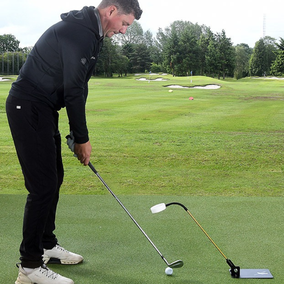 Man practicing golf on a green course with trees in the background