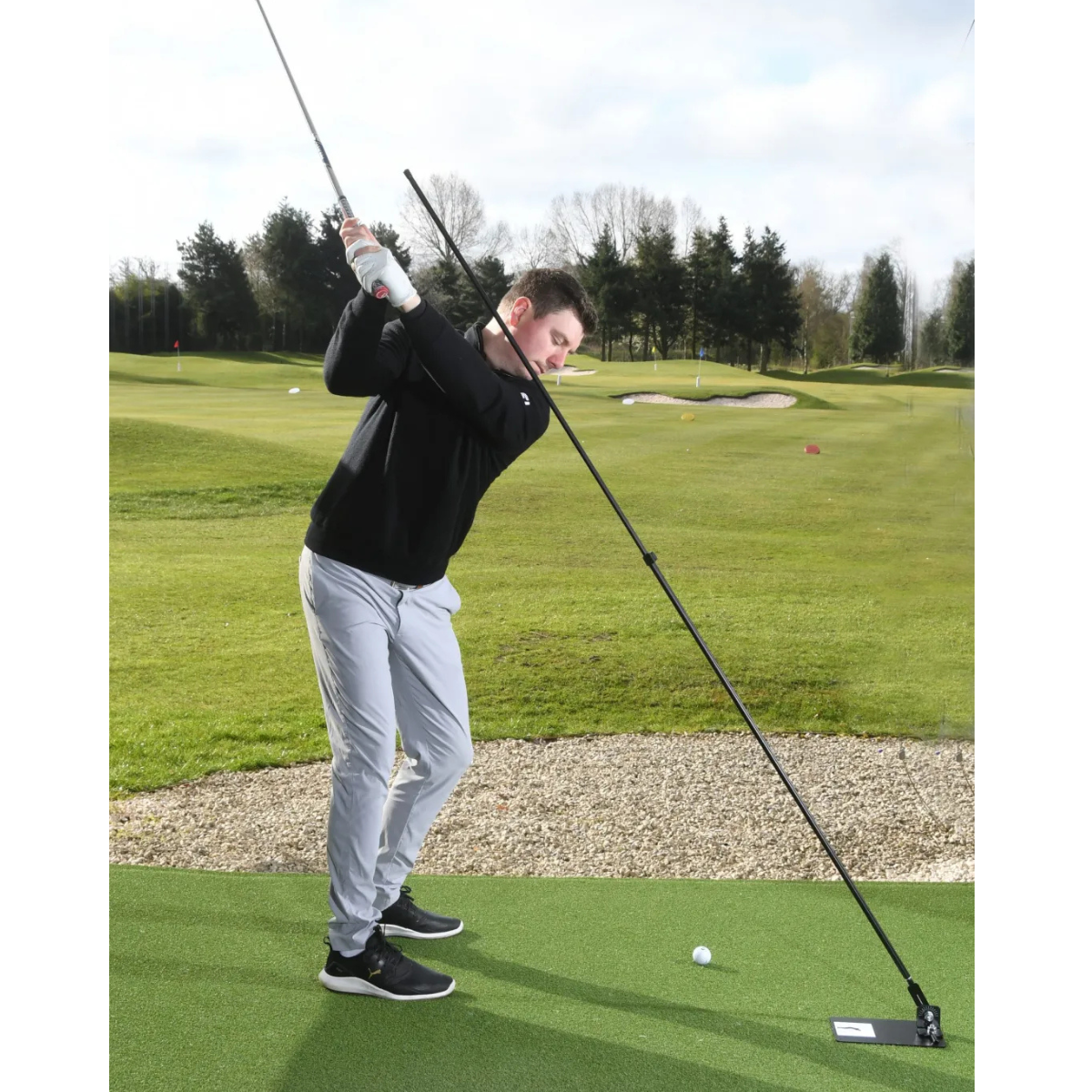 Person playing golf with the Swing Plate on a green course with trees in the background