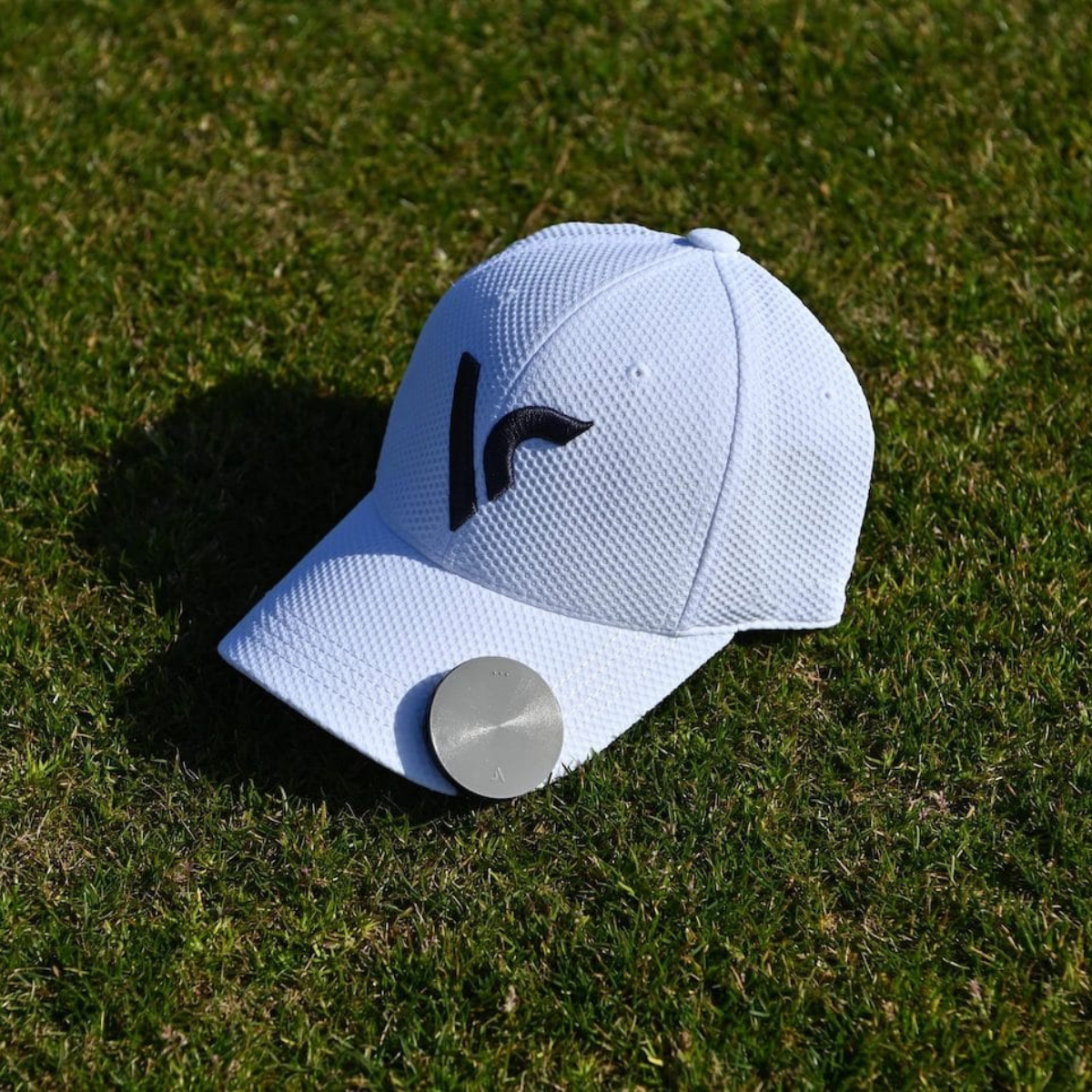 Voice Caddie VC4 clippled on a white cap with a black logo on grass